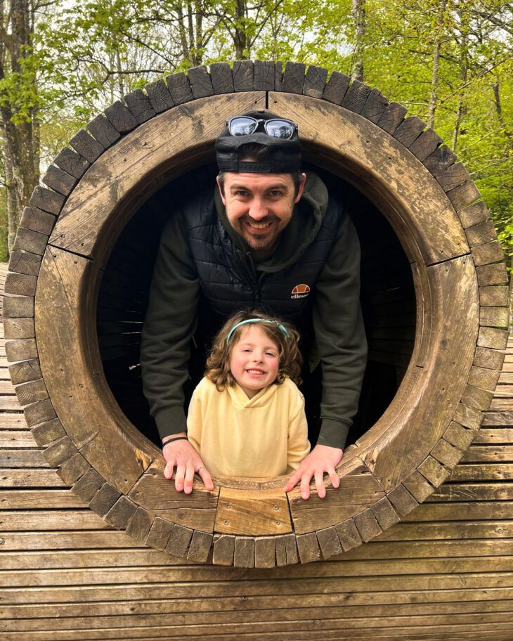 A father and young daughter smile in a tunnel.