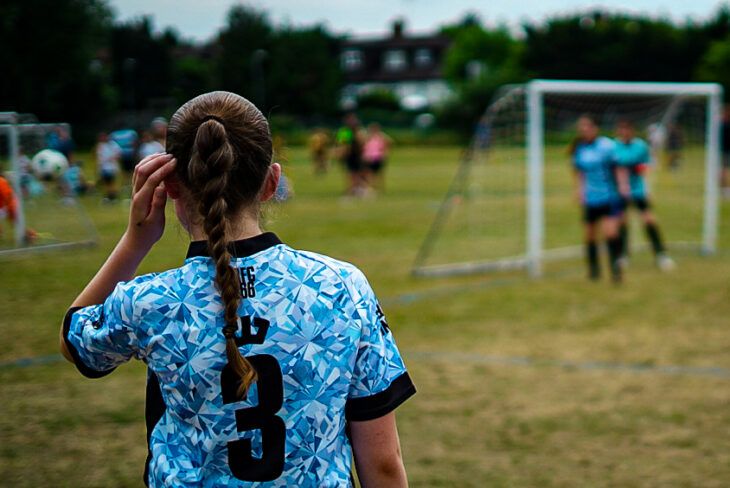 A girl with her back to the camera looks out at the football tournament