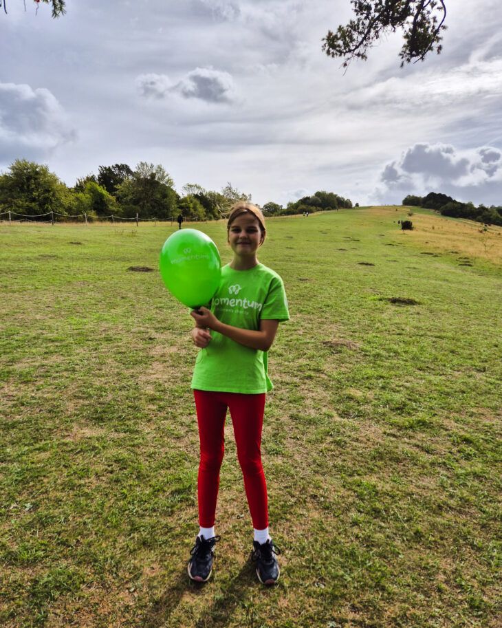 Momentum Young Ambassador stands on Box Hill with a green balloon.