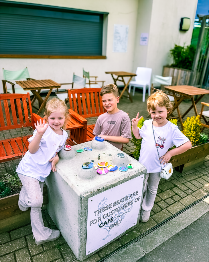 Three children - two girls and a boy smile as they paint pebbles at a Momentum event.