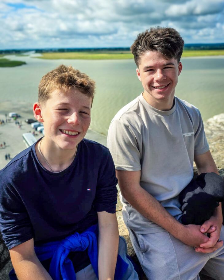 Two teenage brothers sitting next to each other smiling on holiday.
