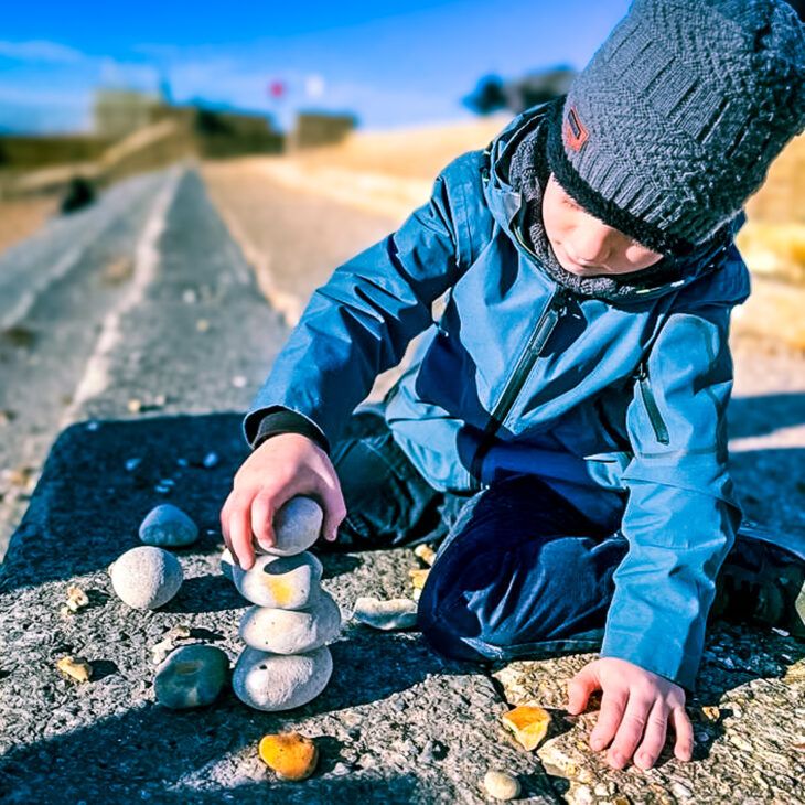 A Momentum supported child sitting outside stacking pebbles on a respite break.