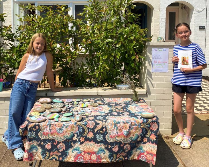 Two girls stand outside a table with pebbles they are selling to raise money for Momentum